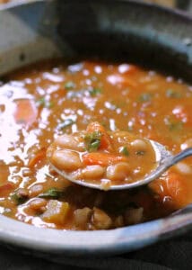 Bowl of bean with bacon soup and a spoon scooping some out.