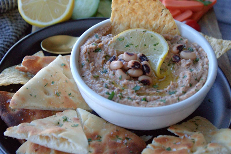 white bowl with black eyed pea hummus garnished with lemon slice and a few whole black eyed peas