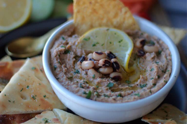 white bowl of black eyed pea hummus served with fresh vegetables and pita chips