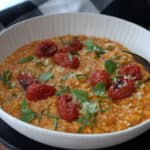shallow white bowl with roasted tomato risotto garnished with roasted cherry tomatoes and basil leaves
