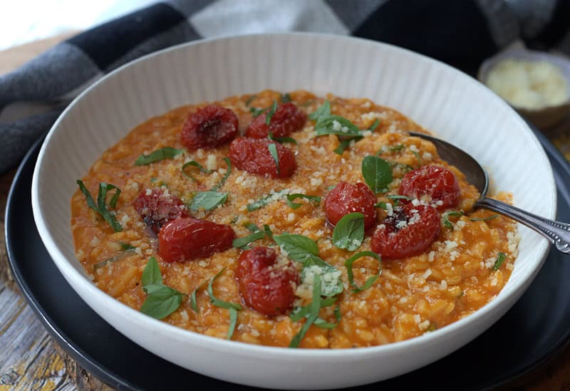 shallow white bowl with roasted tomato risotto garnished with roasted cherry tomatoes and basil leaves