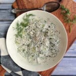 white bowl with creamy cucumber salad finished with fresh cracked black pepper and fresh dill