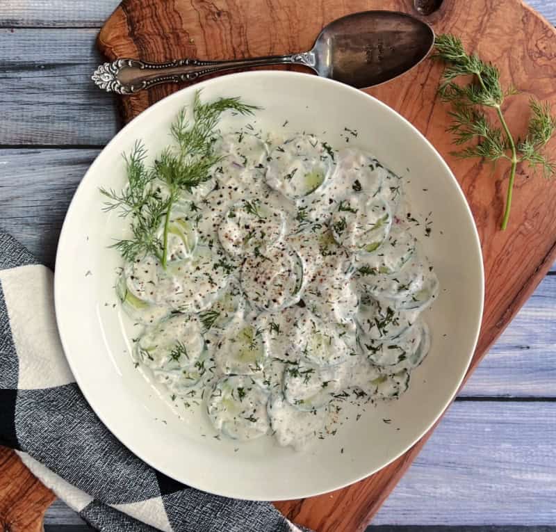 white bowl with creamy cucumber salad finished with fresh cracked black pepper and fresh dill