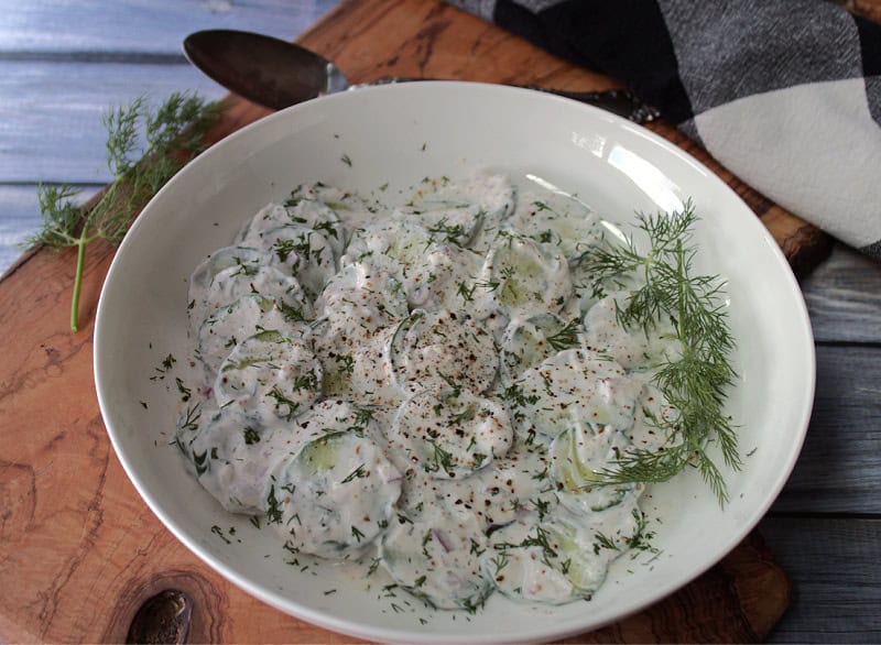 overhead view white bowl with creamy cucumber salad finished with fresh cracked black pepper