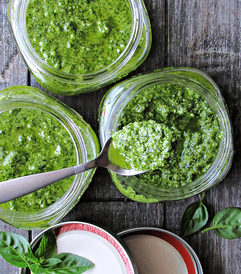 overhead view basil pesto in Mason Jars with spoon scooping some out