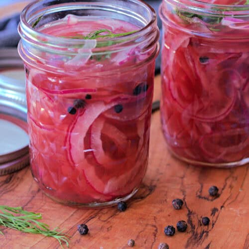 mason jars with pickled red onions and peppercorns on the board near them