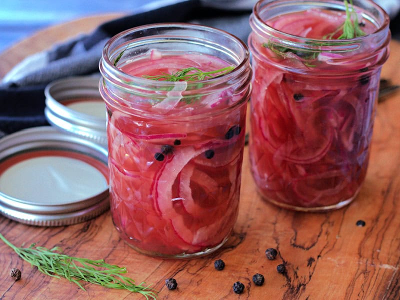 glass jars with pickled red onions with a sprig of dill in each jar