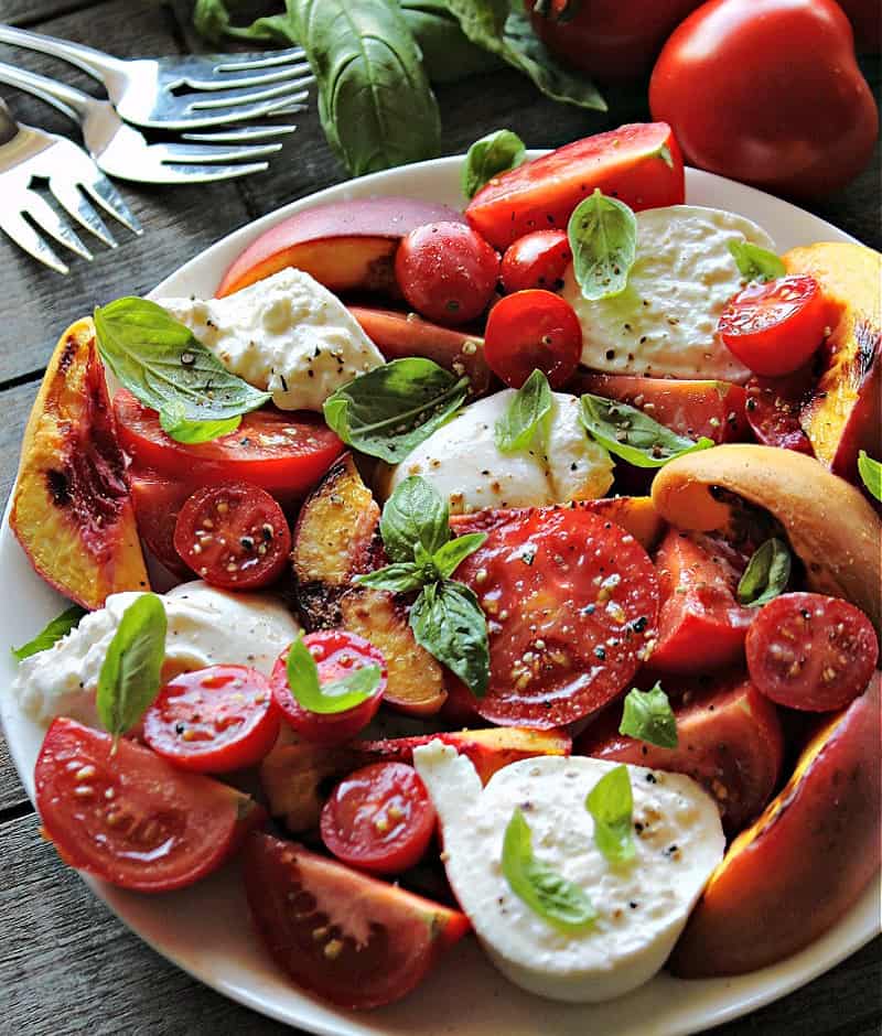 overhead view white plate with grilled peach caprese, small plates and forks on the side