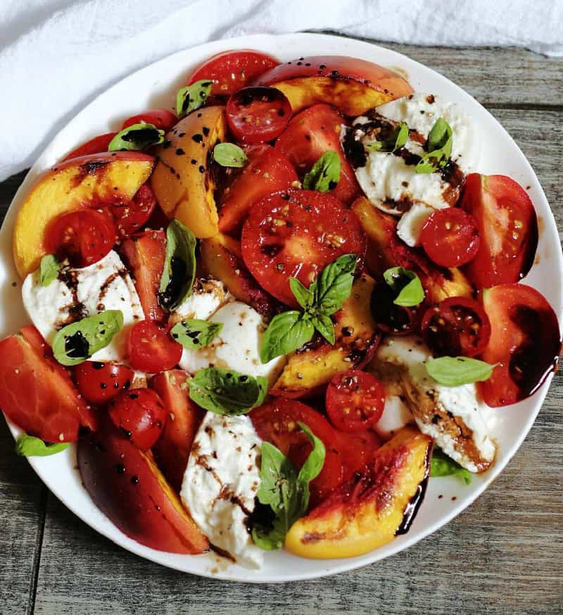overhead view white plate and grilled peach caprese with white napkin in foreground