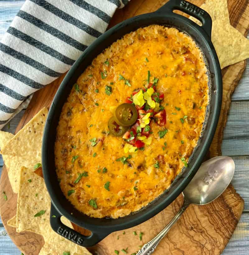 overhead view black casserole dish and cheesy enchilada dip garnished with diced tomatoes and jalapenos