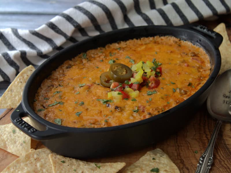 overhead view cheesy enchilada dip in black asserole dish garnished with diced tomatoes