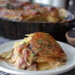 white plate with serving of scalloped potatoes and ham. black casserole dish in the background