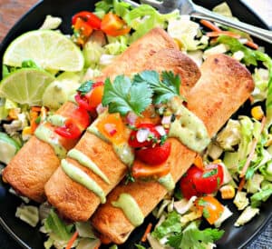 overhead view air fryer chicken taquitos on a black plate garnished with avocado crema