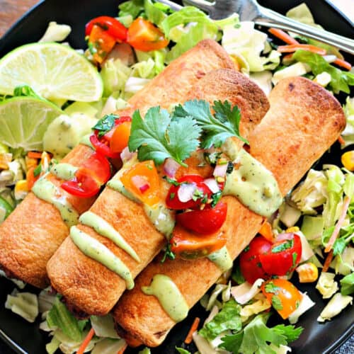 overhead view air fryer chicken taquitos on a black plate garnished with avocado crema