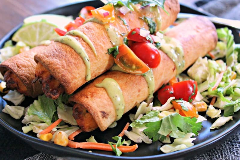 black plate with 3 air fryer chicken taquitos drizzled with avocado crema