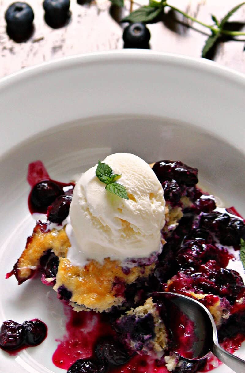 shallow white bowl with blueberry cobbler and dollop of ice cream