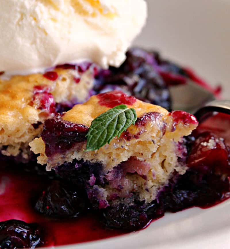 overhead view blueberry cobbler in shallow white bowl with ice cream