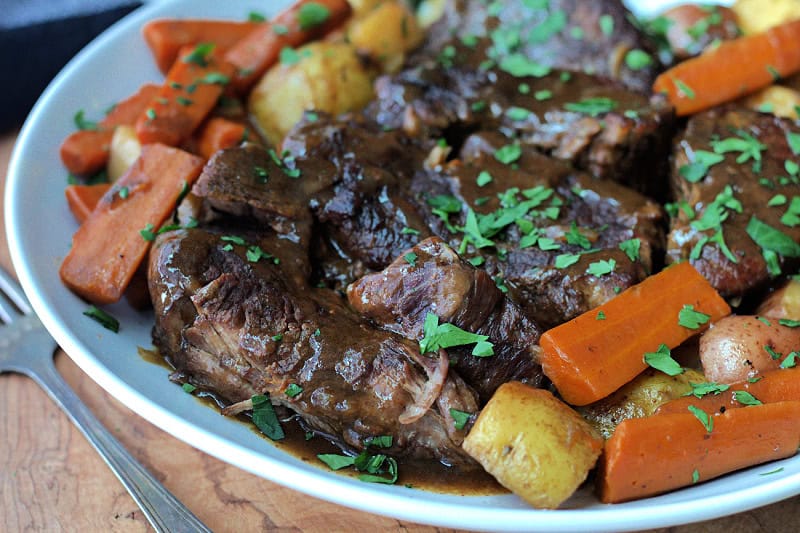 slow cooker pot roast on white platter with carrots and potatoes drizzled with gravy