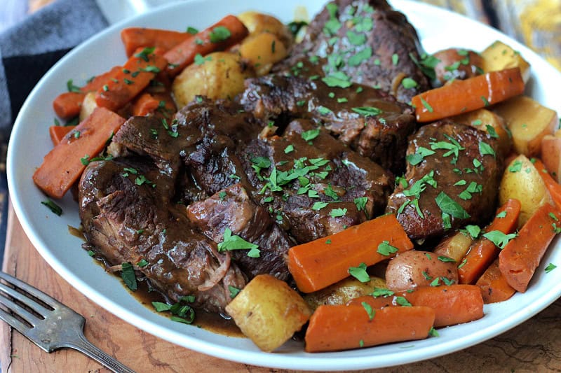 white plate with slow cooker pot roast, carrots, potatoes and gravy