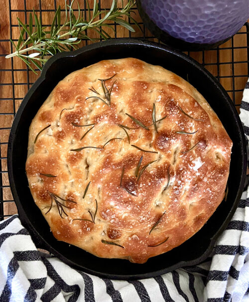 whole loaf of focaccia bread, striped towel and sprigs of rosemary