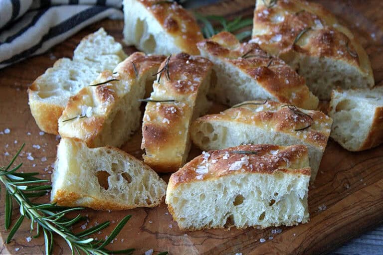 cutting board with sliced focaccia bread and sprigs of rosemary