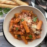 overhead view - white bowl with creamy sausage rigatoni served with crispy breadsticks