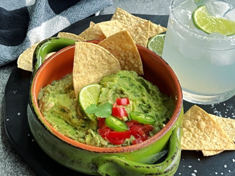 green bowl with easy homemade guacamole garnished with diced tomatoes and served with classic margarita
