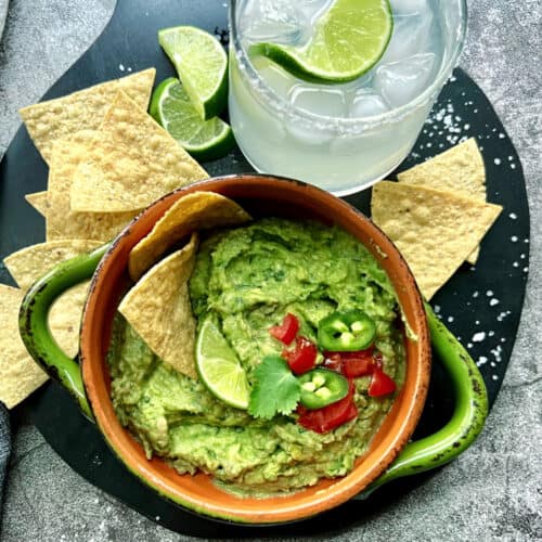 overhead view - green bowl with easy homemade guacamole, tortilla chips and a classic margarita