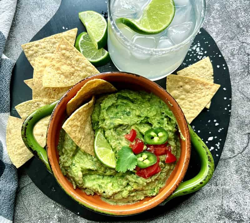 overhead view - green bowl with easy homemade guacamole, tortilla chips and a classic margarita