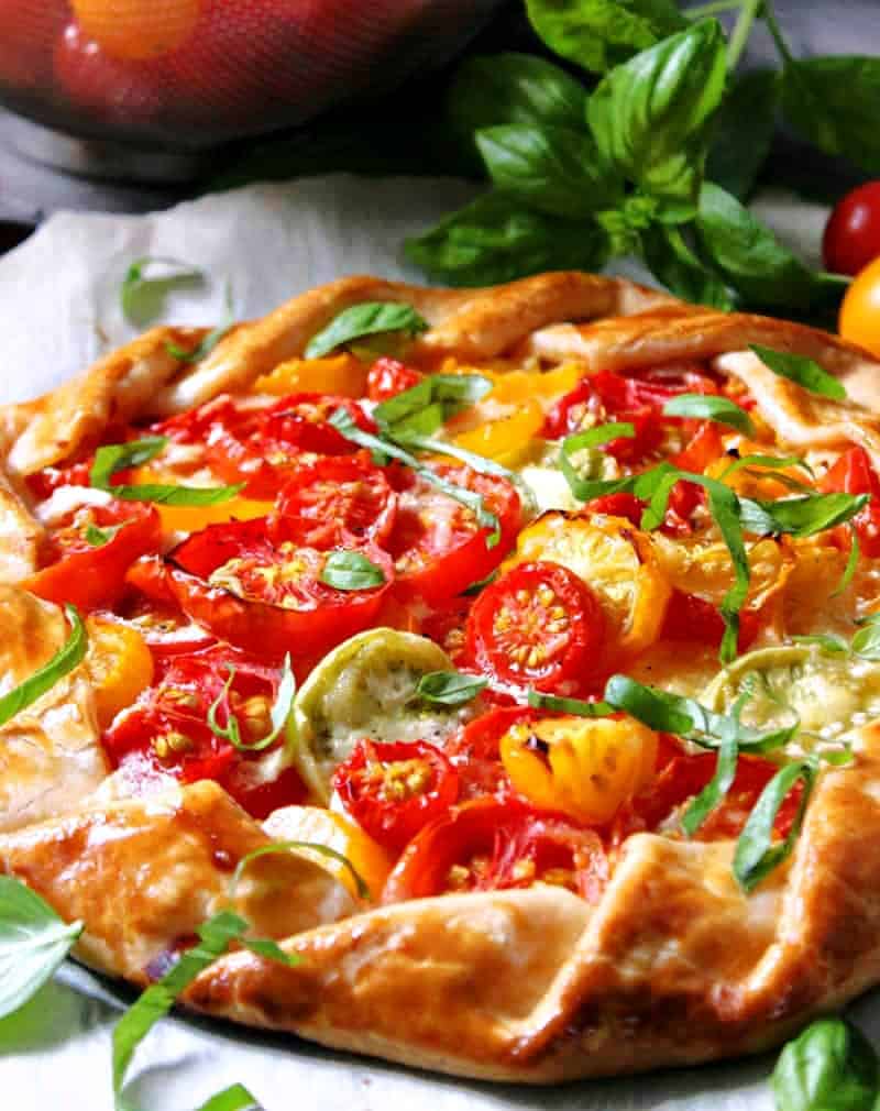 tomato galette on parchment paper with basil sprig nearby