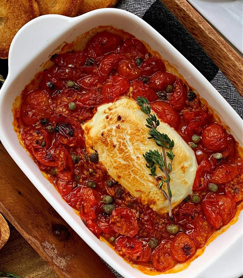 white baking dish with baked goat cheese tomato dip garnished with thyme sprig