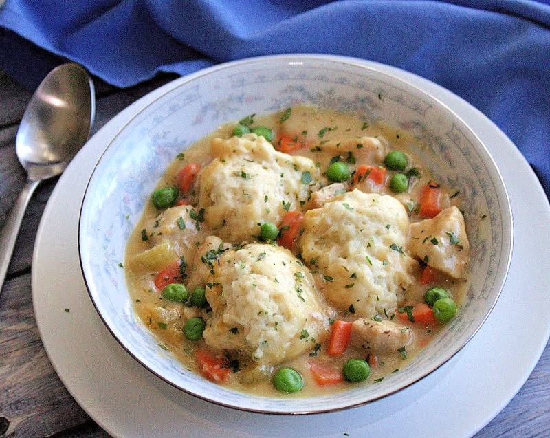 white bowl with easy chicken and dumplings plus bright blue napkin and spoon nearby