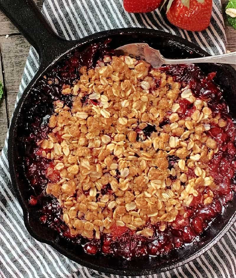 cast iron skillet with Triple Berry Crisp and serving spoon scooping some out