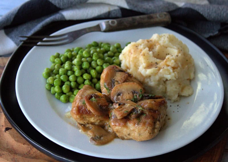 white plate with cheesy baked chicken, mashed potatoes and green peas