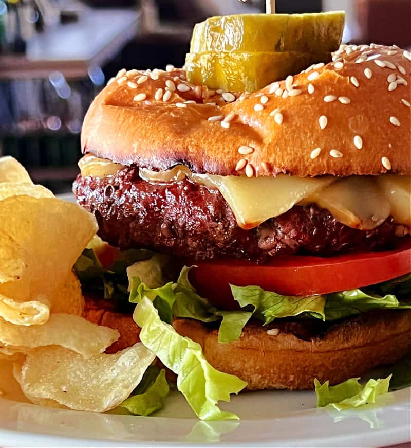 best grilled cheeseburger shown with lettuce, tomato, pickles and a side of potato chips