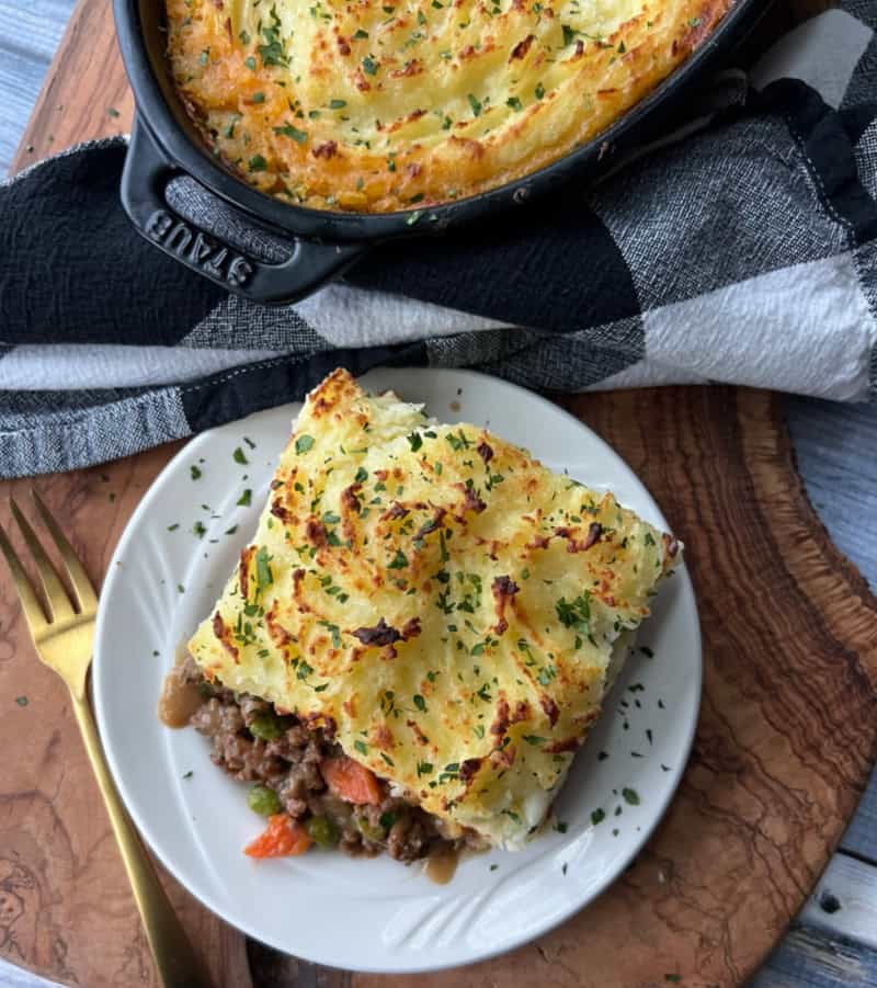 White place with slice of Shepherd's Pie, casserole dish in the background