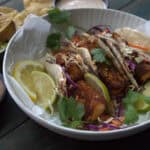 white plate with 3 baja fish tacos served with sliced lemon and lime