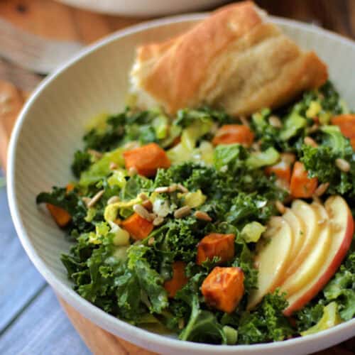 white bowl with fall kale salad and wedge of crusty bread.