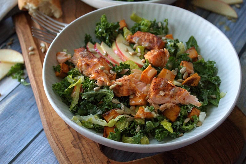 fall kale salad with pieces of cooked salmon and side of crusty bread