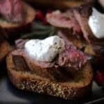 closeup of steak bites crostini topped with a dollop of horseradish cream and fresh cracked black pepper