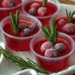 white tray with christmas jello shots garnished with sugared cranberries and sprig of rosemary