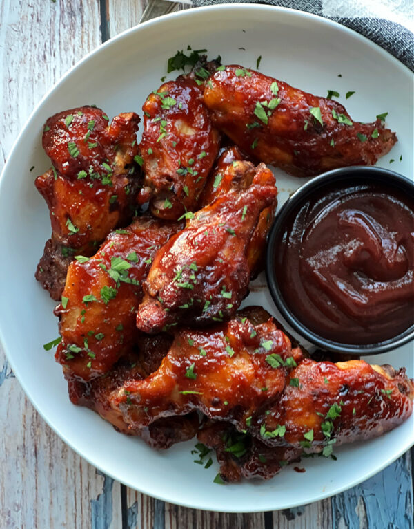 overhead view - white bowl with 3 ingredient crockpot bbq chicken wings garnished with parsley