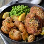 black plate with air fryer chicken and potatoes served with green peas and lemon slices