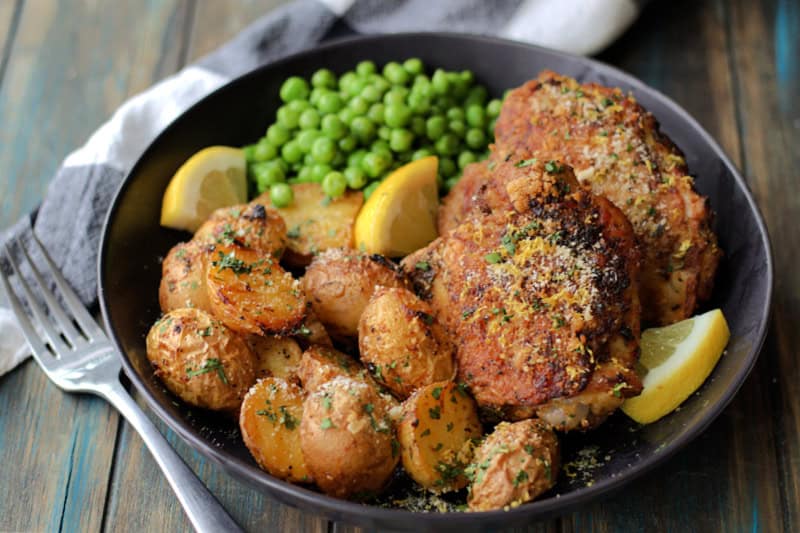 black plate with air fryer chicken and potatoes served with green peas and lemon slices