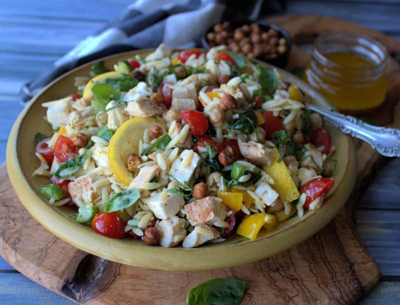 yellow bowl with lemon chicken orzo salad garnished with basil leaves