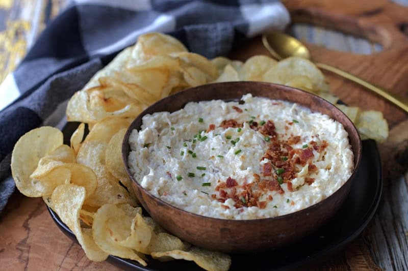 overhead view - copper bowl with smoked gouda cheese dip garnished with crumbled bacon and chives surrounded by potato chips