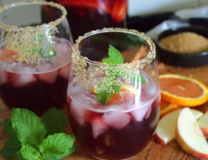 two glasses of Thanksgiving Sangria garnished with mint leaves and slices of apple nearby