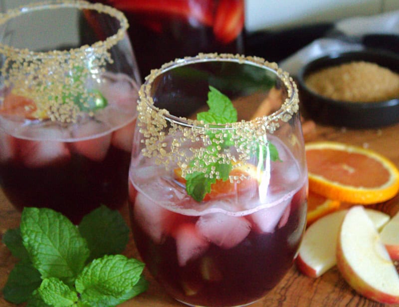 two glasses of Thanksgiving Sangria garnished with mint leaves and slices of apple nearby