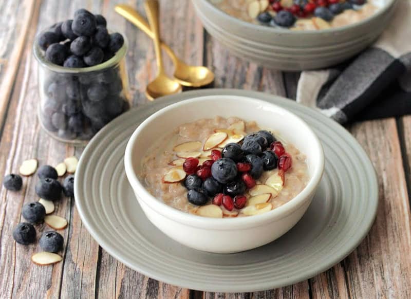 white bowl with slow cooker oatmeal topped with blueberries and pomegranate seeds