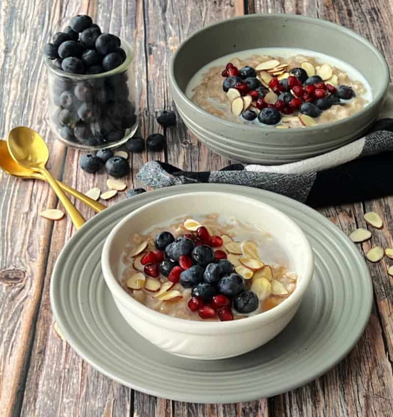 two bowls of slow cooker oatmeal topped wtih blueberries and pomegranate seeds